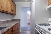 Located at 9001 Patterson Ave in Richmond, Virginia, this single-floor unit offers a clean and functional layout suited for everyday living. The living area is generously proportioned, featuring wall-to-wall beige carpeting, neutral white walls, and a window that allows natural light to brighten the space. A door leads to an additional room or closet, adding practical storage options. The adjacent bedroom is similarly carpeted and features a double window fitted with blinds, providing views of the surrounding outdoor greenery and allowing ample daylight to fill the room. The kitchen is efficiently designed with warm-toned wooden cabinetry, a double stainless steel sink, stone-patterned laminate countertops, and tile flooring. It is equipped with a white gas range and a full-size refrigerator, offering all essential appliances in a compact, easy-to-navigate space. The bathroom features classic tile work surrounding a full-size soaking tub with a shower, complemented by tile flooring and standard fixtures. Throughout the unit, the consistent use of neutral tones and carpeted living spaces creates a cohesive, understated ambiance. The floor plan, as seen in the overhead model view, reflects an efficient use of space with clearly defined areas for living, cooking, and bathing.