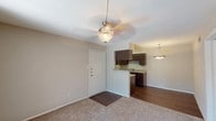 Located at 9001 Jones Rd in Houston, TX, this single-story unit offers a practical and well-organized layout across its living spaces. The main living area features neutral-toned walls, plush carpeting, and a ceiling fan with integrated lighting, creating a comfortable and functional environment. A front entry door opens directly into this space, which flows seamlessly toward the kitchen.

The galley-style kitchen is a standout feature, outfitted with rich dark espresso cabinetry lining both walls, light-toned countertops, a double-basin sink, and black appliances including a range and refrigerator. Wood-look flooring runs throughout the kitchen, adding warmth and contrast to the cabinetry. A pendant light fixture overhead provides focused illumination.

The bedroom is generously proportioned with soft carpeting, neutral walls, and a window fitted with blinds that allows natural light to filter in. A separate view reveals a sliding glass door with vertical blinds that opens to an outdoor area with greenery, enhancing the sense of connection to the outdoors.

The bathroom is clean and efficiently designed, featuring a full-size soaking tub with a tiled shower surround, wood-look flooring, a granite-topped vanity, and dark cabinetry for storage. Overall, the unit presents a cohesive, move-in-ready aesthetic with consistent finishes throughout.