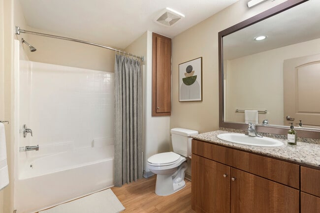 Renovated Package I bath with oak cabinetry, beige speckled granite countertops, and hard surface flooring - Avalon San Dimas