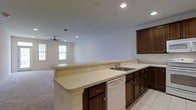 Located at 12001 Old Vine Blvd in Lewes, Delaware, this single-floor home offers a functional and welcoming layout designed for comfortable everyday living. The open-concept design seamlessly connects the kitchen and living area, creating a spacious and airy atmosphere throughout. The kitchen is a standout feature, equipped with rich dark cabinetry that provides generous storage, light-toned countertops, a double-basin sink, and a built-in dishwasher. A broad peninsula counter extends the workspace and serves as a natural divider between the kitchen and the adjoining living area, making it ideal for casual dining or entertaining. Recessed lighting throughout the ceiling ensures consistent illumination, while tile flooring in the kitchen transitions into carpeted flooring in the living space. The living area is fitted with a ceiling fan and benefits from natural light streaming in through multiple windows. The clean white walls and neutral color palette throughout contribute to a bright, move-in ready environment. The single-level layout enhances accessibility and ease of navigation, making this home a practical and inviting residence in the Lewes community.