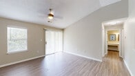 Located at 1015 King George Blvd in Savannah, GA, this single-floor, one-bedroom unit offers a well-organized layout with modern finishes throughout. The living room features light wood-look flooring, a ceiling fan with light fixture, vaulted ceilings that lend an open feel, and a sliding glass door fitted with vertical blinds that opens to a private balcony with lush greenery views. A side window further enhances the natural light in the space. The galley-style kitchen is efficiently designed with crisp white cabinetry, light countertops, and stainless steel appliances including a refrigerator, range, and built-in microwave. The layout maximizes storage and counter space, flowing naturally toward the rest of the unit. The bedroom is generously sized with plush wall-to-wall carpeting, a textured ceiling, and a sliding glass door providing additional outdoor access. Two separate doors lead to a dedicated closet and an additional room, adding to the functional storage of the space. A dedicated laundry room houses a full-size top-loading washer and dryer with overhead wire shelving. Additional areas include a versatile room with wood-look flooring and warm neutral-toned walls, suitable for a variety of uses. Throughout, the unit maintains a clean, neutral palette with white trim and beige tones.
