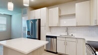 Located at 1155 Park Ln in Davenport, Florida, this single-story unit offers a clean, contemporary design with a cohesive neutral palette and modern finishes throughout. The kitchen serves as a central highlight, showcasing crisp white cabinetry that extends floor to ceiling, providing generous storage. A classic white subway tile backsplash adds texture and character, while light quartz countertops offer ample prep space. A freestanding island with a matching quartz surface anchors the layout, ideal for casual dining or additional workspace. The suite of stainless steel appliances—including a French door refrigerator, electric range, built-in microwave, and dishwasher—delivers a polished, functional cooking environment. Pendant lighting above the island adds a refined touch. Light wood-style plank flooring runs throughout the main living areas, lending warmth and visual continuity. The living area is well-proportioned, featuring a ceiling fan and windows dressed with horizontal blinds that allow natural light to filter in. The bathroom is finished with large-format wall tile surrounding a full soaking tub and shower combination, complemented by a white vanity and the same wood-style flooring. The overall ambiance is bright, clean, and move-in ready.