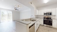 Located at 3855 Avalon Park E Blvd in Orlando, Florida, this single-floor residence offers a well-designed, open-concept layout with a neutral color palette and a clean, modern aesthetic throughout.

The kitchen serves as a central feature of the living area, showcasing granite countertops, white raised-panel cabinetry with brushed nickel hardware, and a full suite of stainless steel appliances including a range, over-the-range microwave, dishwasher, and refrigerator. A peninsula with a double basin sink and a breakfast bar overhang connects the kitchen to the main living space, promoting an open and functional flow. The living area features wood-look plank flooring, crown molding, a ceiling fan with light fixture, and a sliding glass door that brings in natural light and provides outdoor access.

The bedrooms offer plush carpeting, ceiling fans, and windows with blinds that allow for natural light while maintaining privacy. The bathroom is finished with granite countertops, white cabinetry, wood-look flooring, and a full tub-shower combination. The overall ambiance is bright, clean, and move-in ready, with consistent finishes carried throughout the space.