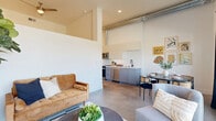 Located at 251 6th St in the heart of downtown Sacramento, this modern 1-bedroom, 1-bathroom unit showcases an industrial-chic aesthetic with soaring ceilings, polished concrete floors, and an open, airy layout. The combined living, dining, and kitchen area forms the heart of the home, where exposed ductwork overhead adds an urban character. The kitchen is outfitted with sleek grey lower cabinetry, crisp white upper cabinets, a white subway tile backsplash, stainless steel appliances including a range, microwave, dishwasher, and refrigerator, and clean white countertops. The living area benefits from generous natural light and direct access to a private balcony through large glass doors, offering open views of the Sacramento skyline and surrounding landscape. A well-lit hallway with recessed lighting connects the main living spaces to the private bedroom, bathroom, closet, and in-unit laundry. The bathroom features a soaking tub with shower combo, white subway tile surround, a floating vanity with white countertop and matte black fixtures, built-in shelving, and a large mirror. Throughout, the consistent use of white walls and concrete flooring creates a cohesive, contemporary atmosphere well-suited for urban living.