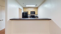 Located at 900 Poplar Forest Rd in Farmville, Virginia, this single-floor unit offers a straightforward and functional layout designed for comfortable everyday living. The entryway opens into a spacious living area finished with warm-toned wall-to-wall carpeting and clean white walls, creating a bright and neutral backdrop throughout. Adjacent to the living space, a hallway connects the various rooms, maintaining an easy flow across the floor plan. The kitchen is positioned as a central feature, equipped with light wood cabinetry, dark countertops, and a full suite of black appliances including a refrigerator, electric range, and over-the-range microwave. A recessed overhead light fixture provides ample illumination, and a breakfast bar-style counter separates the kitchen from the living area. The bedrooms are generously sized, each featuring plush carpeting, white walls, and windows fitted with horizontal blinds that allow for natural light and privacy. The bathroom is cleanly appointed with tile flooring in a warm neutral tone, a single-sink vanity with wood cabinetry, a full-size tub and shower combination, and a well-lit mirror above the vanity. Overall, the unit presents a clean, move-in ready environment with a simple and cohesive aesthetic throughout.