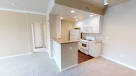 This single-floor residence offers a thoughtfully designed layout with a warm, neutral color palette throughout. The kitchen serves as a central feature, showcasing white shaker-style cabinetry lining both walls, light-toned countertops, and a suite of white appliances including a gas range, over-the-range microwave, and refrigerator. Recessed lighting illuminates the space, while rich wood-look flooring adds contrast and warmth underfoot. A peninsula extends into the adjoining area, providing additional counter space and creating a natural transition into the living area.

The living area is carpeted and benefits from crown molding and a ceiling fan, lending a polished feel. A large sliding glass door fitted with vertical blinds invites an abundance of natural light and provides outdoor access. Adjacent bedrooms are also carpeted and receive generous natural light through windows dressed with vertical blinds. One bedroom features crown molding and a ceiling fan, adding to its comfort.

The bathroom is well-appointed with a full soaking tub and shower combination, wood-look flooring, and built-in open shelving for convenient storage. A hallway connects all rooms, maintaining a practical and cohesive flow throughout the residence.