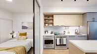 Located at 1575 Queen St E in Toronto's Leslieville neighbourhood, this thoughtfully designed 2-bedroom, 2-bathroom unit makes excellent use of its compact footprint. Light wood flooring runs throughout, complementing a bright, white palette that enhances the sense of openness across the single floor.

The entryway welcomes you with a built-in bench and contemporary wall art, leading into the open-concept living and kitchen area. The kitchen is equipped with stainless steel appliances, including a full-sized range, light wood cabinetry, open shelving, and white countertops. A sliding glass partition with black framing separates the primary bedroom, which features direct views of the kitchen and living space, adding a modern, flexible character to the layout.

The living room is anchored by large sliding glass doors that open onto a private balcony, allowing generous natural light and urban views. The second bedroom includes a window with neighbourhood views, a built-in sliding closet, and clean white walls. Both bathrooms are finished with large-format light grey tiles and matte black fixtures — one featuring a glass-enclosed walk-in shower, and the other a soaker tub with a shower curtain. The overall ambiance is contemporary, clean, and efficiently designed.