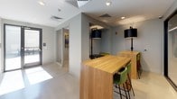 This contemporary single-floor office space is thoughtfully designed to support a variety of work styles, blending open collaboration areas with private enclosed spaces. The layout features a central open area anchored by a natural wood bar-height communal table paired with green upholstered stools and black pendant lighting, creating an inviting hub for informal work and conversation. A colorful, large-scale typographic mural adds a vibrant focal point to the main area, infusing the space with creative energy.

Glass-walled partitions with black frames divide the open floor plan while maintaining visual connectivity and allowing natural light to flow throughout. A private meeting room offers a more intimate setting, finished with textured geometric wallcovering, soft teal upholstered chairs, and a round marble-top table — ideal for focused discussions. An additional enclosed room with a frosted glass door provides flexibility for private use.

The flooring transitions between polished concrete and carpet, lending each zone its own distinct character. Neutral gray walls, recessed lighting, and clean white trim maintain a cohesive, professional aesthetic throughout. The overall ambiance is modern and functional, balancing open-plan energy with quiet, purpose-driven spaces suited for a dynamic professional environment.