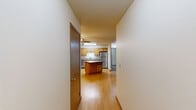 This single-floor residence offers a practical and comfortable layout across two bedrooms, two bathrooms, and a thoughtfully arranged set of living spaces. The kitchen serves as a functional centerpiece, featuring warm oak cabinetry, granite-style countertops, stainless steel appliances including a range, microwave, and refrigerator, and a central island that provides additional prep and storage space. Light hardwood flooring runs throughout the kitchen and entry areas, lending warmth and continuity to the space. The open kitchen connects naturally toward the living room, which is carpeted and filled with natural light through a large set of windows and a glass door that opens to an exterior patio or balcony area. Both bedrooms are carpeted and neutral in tone, offering versatile spaces for rest or use. The primary bedroom is generously sized, while the second bedroom provides comfortable secondary accommodations. One bedroom features a vaulted ceiling, adding an airy sense of height. Both bathrooms are finished with oak vanities, granite-style countertops, tile flooring, and bright vanity lighting. One bathroom includes a full tub-shower combination. A dedicated laundry area and in-unit HVAC system round out the practical amenities of this well-maintained residence.