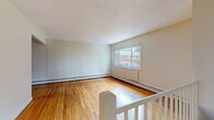 This single-floor unit in Manchester, Connecticut offers a well-organized layout with a variety of functional living spaces. Warm-toned hardwood flooring runs throughout the main living areas and bedrooms, lending a cohesive and inviting character to the interior. A staircase with a white-painted railing provides access to the unit, opening into a generously sized living area bathed in natural light from a large front-facing window.

The kitchen is equipped with stainless steel appliances, including an electric range, over-the-range microwave, and dishwasher. Warm wood cabinetry, granite-style countertops, and a subtle tile backsplash complete the space, which also features light luxury vinyl plank flooring for easy maintenance. A window above the sink brings in additional natural light.

Multiple bedrooms are present, each featuring hardwood floors, neutral walls, and windows that allow ample daylight. Baseboard heating units run along the perimeter of most rooms, providing consistent warmth throughout.

The bathroom includes a full tub-shower combination with white tile surround, a dark wood vanity with a white countertop, tile flooring, and a window for ventilation and natural light. Overall, the unit presents a clean, functional living environment suitable for everyday comfort.