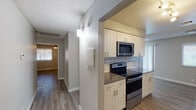 This single-floor residence showcases a thoughtfully updated interior with consistent wood-look flooring and neutral tones throughout. The kitchen is a standout feature, designed in a galley style with white shaker cabinetry, sleek dark countertops, classic subway tile backsplash, and a full suite of stainless steel appliances including a refrigerator, electric range with microwave above, and dishwasher. Track lighting illuminates the workspace, while a hallway connects the kitchen to the rest of the home. The open living area is centered around a clean-lined fireplace and features a ceiling fan with light fixture, providing both comfort and style. Notably, the space also accommodates an in-unit washer and dryer. The bedrooms are generously sized, each with ceiling fans, natural light from blinds-fitted windows, and closet storage. Neutral gray walls create a calm, versatile backdrop throughout. The bathrooms are finished with white vanity cabinetry, dark countertops, wood-framed mirrors, and brushed nickel fixtures. One bathroom includes a walk-in shower with white tile surround. Textured ceilings are present throughout the home, adding architectural character to the overall design.