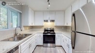 Located at 4849 Manzanita Ave in Carmichael, CA, this 2-bedroom, 2-bathroom unit at Brookside Apartments features a thoughtfully designed single-floor layout with contemporary finishes throughout. The open living area is anchored by a corner fireplace with stone surround and is finished with warm wood-tone laminate flooring, creating an inviting atmosphere. Natural light filters in through slatted blinds, complementing the neutral gray wall tones found throughout the unit. The kitchen is well-appointed with white shaker-style cabinetry, light granite-look countertops, stainless steel appliances including a refrigerator and range, and a stainless steel sink — all set on light wood-tone flooring. Both bedrooms are generously sized, featuring plush carpeting, large windows with blinds, and access to adjacent bathrooms. Each bathroom is finished with wood-look tile flooring, a white shaker-style vanity, a framed mirror with contemporary vanity lighting, and clean white fixtures. The cohesive design palette of soft grays and whites throughout creates a clean, modern aesthetic well-suited for comfortable everyday living.