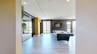 Located at 127 W Pomona Ave in Monrovia, CA, this contemporary single-floor space offers a generous and thoughtfully designed layout ideal for gathering and entertaining. The interior features light hardwood flooring throughout, with bold accent walls in deep charcoal and warm golden yellow that lend a modern, curated aesthetic. The main living area is anchored by floor-to-ceiling glass windows and sliding doors that flood the space with natural light and frame views of the surrounding neighborhood. A wet bar with bar seating and open shelving adds a functional social element to this room. A secondary living area features dramatic corner glass walls on two sides, creating an immersive, light-filled lounge with panoramic outdoor views. A connecting hallway with vibrant yellow accent walls guides visitors through the space, and an ADA-accessible bathroom with clean, neutral finishes rounds out the interior. The space truly distinguishes itself with its expansive outdoor terraces. A covered lounge area with polished concrete floors and modern seating transitions seamlessly to an open rooftop deck furnished with a dining table and shaded umbrella, offering open-sky views. A private courtyard entry accented with blooming bougainvillea adds a welcoming, resort-like arrival experience.