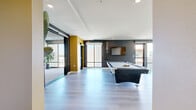 Located at 127 W Pomona Ave in Monrovia, CA, this contemporary single-floor space offers a generous and thoughtfully designed layout ideal for gathering and entertaining. The interior features light hardwood flooring throughout, with bold accent walls in deep charcoal and warm golden yellow that lend a modern, curated aesthetic. The main living area is anchored by floor-to-ceiling glass windows and sliding doors that flood the space with natural light and frame views of the surrounding neighborhood. A wet bar with bar seating and open shelving adds a functional social element to this room. A secondary living area features dramatic corner glass walls on two sides, creating an immersive, light-filled lounge with panoramic outdoor views. A connecting hallway with vibrant yellow accent walls guides visitors through the space, and an ADA-accessible bathroom with clean, neutral finishes rounds out the interior. The space truly distinguishes itself with its expansive outdoor terraces. A covered lounge area with polished concrete floors and modern seating transitions seamlessly to an open rooftop deck furnished with a dining table and shaded umbrella, offering open-sky views. A private courtyard entry accented with blooming bougainvillea adds a welcoming, resort-like arrival experience.