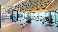 Located at 9 Harrington St in downtown Raleigh, NC, this contemporary fitness and wellness center delivers a premium exercise experience across a generously sized single floor. The facility is thoughtfully designed with distinct zones to accommodate a wide range of workout styles and fitness goals.

The main gym floor features rubber flooring and an impressive geometric coffered ceiling with integrated linear lighting, creating an elevated, modern aesthetic. Floor-to-ceiling glass walls flood the space with abundant natural light and offer sweeping views of the Raleigh cityscape and tree canopy, providing an inspiring backdrop for every workout. The area is outfitted with professional-grade True-brand cardio machines including treadmills and ellipticals, a multi-station cable machine, free weight benches, and a comprehensive dumbbell rack backed by full-length mirrors.

A dedicated functional training zone includes a multi-purpose rig equipped with TRX suspension systems, medicine balls, and kettlebells, supporting dynamic and group-style training. Frosted glass partition walls with artistic patterned graphics delineate a separate studio room, ideal for group fitness classes or personal training sessions, featuring light wood flooring and colorful fitness accessories.

The facility is accessed through a welcoming entry foyer marked by bold wellness-branded glass doors, a reception storage area, and seating. The overall ambiance is modern, bright, and motivating, reflecting a high-end commitment to health and wellness.