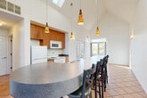 Located at 3139 Professional Dr in Ann Arbor, MI, this single-floor, one-bedroom, one-bathroom residence offers a thoughtfully designed layout that maximizes its well-proportioned footprint. The architectural centerpiece is the open-concept kitchen and dining area, where dramatic vaulted ceilings soar overhead and skylights flood the space with natural light. A curved, dark stone-topped kitchen island with bar seating anchors the room, complemented by warm wood cabinetry, white appliances, and tile flooring in a classic terracotta tone. Artistic pendant lights hang at varying heights, adding visual character to the airy volume. Large windows along the dining area frame outdoor views and further enhance the bright, open ambiance. The living area continues the tile flooring and benefits from abundant natural light streaming through generous windows with tree-lined views. The bedroom features light hardwood flooring, a built-in closet with bi-fold doors, and wall sconce lighting, creating a calm and comfortable retreat. The bathroom offers a wide vanity with ample cabinetry, a large mirror, and tile flooring. Additional highlights include multiple closets throughout and a dedicated laundry area, providing practical everyday convenience in this well-appointed Ann Arbor residence.