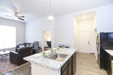 This single-floor residence offers a thoughtfully designed layout that balances comfort and functionality. The kitchen serves as a central highlight, featuring bold dark cabinetry with raised-panel detailing, granite-look countertops, black appliances, and a generous island with seating for several — ideal for casual dining and entertaining. Track lighting and a pendant fixture illuminate the space, while wood-look flooring extends throughout the main living areas.

The living room provides a welcoming gathering space with notably high ceilings that lend an open, airy feel. Bedrooms are carpeted for comfort and each includes a dedicated closet with built-in shelving, a window for natural light, and ample room for furniture and personal belongings. The layout visible in the dollhouse view confirms multiple bedrooms with efficient corridor connections.

Bathrooms are finished consistently with dark vanity cabinetry, light stone-look countertops, and wood-look tile flooring. One bathroom features a walk-in shower, while another serves as a powder-style half bath. A dedicated in-unit laundry area houses a full-size top-load washer and dryer side by side. Abundant cabinetry, including a tall pantry cabinet in the kitchen, provides generous storage throughout the residence.