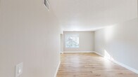 This single-story space is designed with a clean, neutral aesthetic that creates a bright and welcoming atmosphere throughout. The main living areas feature light-toned hardwood-style flooring that extends seamlessly through the open layout, complemented by crisp white baseboards and soft beige walls. A textured ceiling in the main living room adds subtle dimension, while a window at the far end draws in natural light and offers views of surrounding greenery.

The kitchen is a functional and stylish space, equipped with stainless steel appliances including an electric range and over-the-range microwave. Light stone-look countertops contrast with dark cabinetry, and a distinctive vertical shiplap accent wall introduces a modern farmhouse touch. The same shiplap detailing appears in an adjacent area, providing visual consistency across spaces.

The bedrooms are finished with plush, neutral-toned carpet that adds warmth and comfort. Each room offers ample wall space and standard closet access. A hallway bathroom features a white vanity with a single-basin sink and a full tub-shower combination, finished with clean white surrounds and light wood-style flooring. A second vanity area provides additional convenience. The overall ambiance is clean, move-in ready, and well-suited for a variety of furniture arrangements.