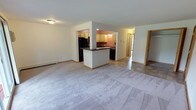 This two-bedroom, one-bathroom unit is thoughtfully laid out across a single floor, offering a comfortable and functional living environment. The open-concept living area features neutral carpet flooring and flows seamlessly into the kitchen via a half-wall peninsula with a dark countertop. Sliding glass doors in the living room fill the space with natural light and open onto a private balcony that overlooks a well-maintained, tree-lined courtyard with mature trees, green lawn, and a walkway — providing a serene outdoor setting.

The kitchen is equipped with light maple cabinetry, dark granite-style countertops, and a full suite of black appliances including a refrigerator, range, microwave, and dishwasher. Tile flooring runs throughout the kitchen and entry areas, complementing the warm-toned accent walls.

Both bedrooms are carpeted and feature warm wood trim, with natural light provided by single windows. Each bedroom includes closet storage — one with a walk-in style closet and another with a bi-fold door closet. A hallway connects the bedrooms to the full bathroom, which includes a tub/shower combination, tile flooring, and a wood-trimmed vanity with a stone-style countertop. Baseboard heating is present throughout the unit.