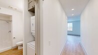 Located at 100 E Chestnut St in Rogers, Arkansas, this well-designed one-bedroom, one-bathroom unit offers a thoughtful layout across a single floor. Light-toned hardwood-style flooring runs throughout, creating a cohesive and clean aesthetic in every room.

The open-concept kitchen and living area serves as the heart of the unit. The kitchen is outfitted with gray shaker-style cabinetry, stainless steel appliances including a range, microwave, and dishwasher, a subway tile backsplash, and a single-basin sink. Large windows bathe the combined living space in natural light while providing views of the surrounding Rogers neighborhood.

The bedroom is a comfortable, well-proportioned space featuring a ceiling fan, a closet, and easy access to the adjoining living area, maintaining an open and connected flow. A hallway connects the main living spaces and includes a dedicated closet housing a stacked washer and dryer unit, adding in-unit laundry convenience.

The bathroom features light wood-style flooring consistent with the rest of the unit, a walk-in shower, a toilet, and a vanity with a framed mirror and taupe cabinetry with brushed nickel hardware. The overall design is clean and modern, with white walls and recessed lighting reinforcing a bright, contemporary ambiance throughout the space.