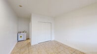 This 230 square foot studio apartment in Hialeah, Florida offers a practical living solution in a compact space. The single-floor layout comprises a main living area and a separate bathroom. The living space is characterized by its neutral white walls and beige tile flooring, creating a clean and bright atmosphere. A notable feature is the large window with horizontal blinds, allowing natural light to flood the room while providing privacy control. The space is equipped with a wall-mounted air conditioning unit for climate comfort. A closet with double doors provides essential storage. The bathroom, while compact, includes a vanity with storage, a toilet, and a bathtub with shower functionality. The entire apartment maintains a consistent design theme with its neutral color palette and practical amenities, making efficient use of the limited square footage.