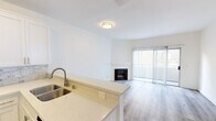 This well-appointed one-bedroom, one-bathroom unit offers a thoughtfully designed open-concept layout that maximizes its compact footprint. The combined kitchen and living area serves as the heart of the space, where a peninsula with light quartz countertops and a double stainless steel sink creates a natural division between the two zones. The kitchen is equipped with stainless steel appliances, including a gas range, over-the-range microwave, and refrigerator, all framed by crisp white shaker cabinetry and a marble-style tile backsplash. Light wood-style flooring flows seamlessly throughout the main living area, contributing to a bright, cohesive aesthetic.

The living area features a fireplace as a focal point and is anchored by a sliding glass door fitted with vertical blinds, providing access to a balcony and drawing in natural light. The bedroom is a comfortably sized retreat with clean white walls and continued wood-style flooring, with convenient access to adjacent spaces. The bathroom includes a tub and shower combination enclosed by sliding glass doors with a clean white tile surround. The overall ambiance is clean, modern, and move-in ready.