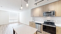 Located at 2311 Dulles Station Blvd in Herndon, Virginia, this single-floor residence offers a thoughtfully designed layout with modern finishes and a clean, contemporary aesthetic throughout. The kitchen is a standout feature, showcasing light wood cabinetry extending to the ceiling, a full suite of stainless steel appliances including a refrigerator, range, microwave, and dishwasher, and a white quartz countertop island with pendant lighting overhead. A classic subway tile backsplash and track lighting complete the space, which flows seamlessly into the open living area via warm hardwood-style flooring. The bedrooms are carpeted and bright, with large windows that invite natural light. One bedroom features built-in open shelving, offering versatile storage options, while another includes a set of double doors leading to a closet. The bathroom is finished with a warm wood vanity, white quartz countertop, a large mirror with overhead vanity lighting, and neutral tile flooring, creating a spa-like atmosphere. Throughout the residence, crisp white walls, black hardware accents, and high ceilings contribute to a bright, airy ambiance. The overall design balances functionality with contemporary style, making this a well-appointed and move-in-ready space.