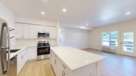 This single-floor unit offers three bedrooms, two bathrooms, and a thoughtfully designed open-concept layout. The kitchen serves as a central hub of the space, featuring white shaker-style cabinetry, sparkling quartz countertops, a large center island, and a full suite of stainless steel appliances including a gas range, built-in microwave, dishwasher, and refrigerator. Open wall shelving adds functional storage while maintaining a clean, contemporary aesthetic. Light hardwood flooring runs throughout the main living areas, enhancing the bright and airy atmosphere created by recessed lighting and natural light from multiple windows.

The living area flows naturally from the kitchen and includes a door with a sidelight panel that provides outdoor access and additional natural light. The primary bedroom offers a comfortable footprint, complemented by a walk-in closet equipped with wire shelving and hanging rods. Additional bedrooms are well-proportioned with windows providing natural light and views of the surrounding greenery. The bathrooms feature quartz vanity countertops, white cabinetry, and decorative patterned tile flooring, adding a subtle design element to the otherwise neutral palette throughout the unit.