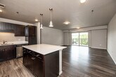 Located at 45 W Jefferson St in Waterloo, Iowa, this one-bedroom, one-bathroom residence offers a well-designed single-floor layout with a thoughtful mix of style and functionality. The open-concept kitchen and living area serves as the heart of the unit, featuring dark shaker-style cabinetry, light quartz countertops, a center island with pendant lighting, and a full suite of stainless steel appliances including a refrigerator, range, microwave, and dishwasher. Wood-style plank flooring flows throughout the main living areas, adding warmth and continuity. The living room is bright and airy, benefiting from a large sliding glass door that opens to a private balcony with outdoor views. The generously sized bedroom is finished with plush carpeting, a window providing natural light, and access to a dedicated walk-in closet. The bathroom features a wide vanity with dark cabinetry, a white countertop, a large mirror, and wood-look tile flooring. Additional spaces include multiple closets, a hallway, and a utility room, maximizing storage and practicality. The unit's neutral color palette and modern finishes create a clean, contemporary ambiance throughout.