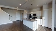 This two-floor home showcases a thoughtfully designed interior centered around a modern, open-concept kitchen. The kitchen is a standout feature, equipped with crisp white cabinetry that extends to the ceiling, providing ample storage space. A large central island with a granite countertop serves as both a functional workspace and a natural gathering point, complete with an integrated sink. Pendant lighting hangs above the island, adding a refined touch to the space.

The kitchen is outfitted with stainless steel appliances, including a refrigerator, range, and microwave, offering a sleek and cohesive aesthetic. The granite countertops carry consistent veining throughout, complementing the neutral, warm-toned walls. Recessed lighting and a tray ceiling detail add architectural interest overhead.

Dark hardwood flooring flows seamlessly from the kitchen into the adjacent open living area, grounding the space with a rich, warm contrast to the lighter cabinetry and walls. The open layout creates a sense of spaciousness and easy flow between areas. The overall ambiance is clean, contemporary, and move-in ready, reflecting a well-planned and polished design.