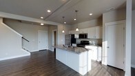 This two-floor home showcases a thoughtfully designed interior centered around a modern, open-concept kitchen. The kitchen is a standout feature, equipped with crisp white cabinetry that extends to the ceiling, providing ample storage space. A large central island with a granite countertop serves as both a functional workspace and a natural gathering point, complete with an integrated sink. Pendant lighting hangs above the island, adding a refined touch to the space.

The kitchen is outfitted with stainless steel appliances, including a refrigerator, range, and microwave, offering a sleek and cohesive aesthetic. The granite countertops carry consistent veining throughout, complementing the neutral, warm-toned walls. Recessed lighting and a tray ceiling detail add architectural interest overhead.

Dark hardwood flooring flows seamlessly from the kitchen into the adjacent open living area, grounding the space with a rich, warm contrast to the lighter cabinetry and walls. The open layout creates a sense of spaciousness and easy flow between areas. The overall ambiance is clean, contemporary, and move-in ready, reflecting a well-planned and polished design.
