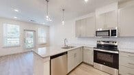 This well-appointed 1-bedroom, 1-bathroom residence offers a thoughtfully designed single-floor layout that maximizes functionality and style. The open-concept living and kitchen area is anchored by a peninsula island topped with granite countertops, complemented by sage-toned shaker cabinetry, a classic white subway tile backsplash, and a full suite of stainless steel appliances including a range, microwave, dishwasher, and refrigerator. Glass pendant lights hang above the island, adding a refined touch. Light-toned wood-style flooring flows throughout the entire residence, contributing to a clean, cohesive aesthetic. Large windows with horizontal blinds fill the living area with natural light and offer views of the surrounding greenery, while a glass-paned entry door enhances the sense of openness. The bedroom is a comfortable, well-lit retreat with a ceiling fan, a large window, and direct access to two closets. The bathroom features a granite-topped vanity with an undermount sink, a soaking tub with a marble-look tiled surround, and recessed lighting. Additional highlights include a dedicated laundry area and a hallway connecting all rooms seamlessly, making this a practical and polished living space.