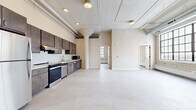Unit 413 at Twelve 22, located in Saint Paul, MN, is a two-bedroom, one-bathroom residence that blends industrial character with contemporary updates. The unit's open layout provides a generous, flowing living area anchored by polished concrete-style flooring that runs throughout the space. Exposed ductwork and structural columns along the ceiling reinforce the building's industrial heritage, while recessed lighting ensures the interior remains bright and functional.

The kitchen runs along one wall and is well-appointed with dark espresso cabinetry extending to the ceiling, light countertops, a stainless steel dishwasher, electric range, and microwave. Ample upper and lower cabinet storage makes this a highly practical cooking space.

Both bedrooms feature large, multi-pane grid windows set against exposed masonry walls, flooding the rooms with natural light and offering open views of the Saint Paul skyline. Each bedroom includes a dedicated closet with built-in shelving and hanging rods for organized storage.

The bathroom continues the unit's design language with a dark wood vanity, light countertop, a large grid window, and a well-lit mirror. An in-unit washer is tucked into a dedicated closet, adding everyday convenience. Overall, the unit delivers an urban, loft-inspired atmosphere with thoughtful modern finishes.