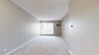 Located at 1417 Valley Lake Dr in Schaumburg, IL, this one-bedroom, one-bathroom unit offers a well-organized single-floor layout with a thoughtful arrangement of living spaces. The living area is generously sized, featuring soft wall-to-wall carpeting, neutral gray-toned walls, and a large sliding window dressed with vertical blinds that floods the room with natural light and provides access to an outdoor view. A wall-mounted air conditioning unit and baseboard heating ensure year-round comfort.

The kitchen is clean and contemporary, outfitted with white shaker-style cabinetry, light quartz countertops, a stainless steel sink, and modern appliances including a stainless steel refrigerator and dishwasher. Light wood-tone flooring ties the kitchen together with a fresh, updated aesthetic.

The bedroom is a comfortable retreat, offering plush carpeting, a ceiling fan, baseboard heating, and a wide bi-fold closet that provides ample storage. The neutral color palette throughout maintains a calm, cohesive feel.

The bathroom is clean and functional, featuring a full-size soaking tub with a shower, crisp white subway tile surround, and chrome fixtures. The entrance completes the layout, offering a practical transition into the living space. Overall, this unit presents a move-in ready, efficiently designed home in a convenient Schaumburg location.