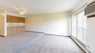 Located at 4605 W Chippewa Cir in Sioux Falls, South Dakota, this single-floor unit offers a practical and efficiently designed layout. The galley-style kitchen is equipped with warm wood cabinetry on both sides, white appliances including an electric range and refrigerator, a double-basin stainless steel sink, and light tile flooring — providing ample storage and counter space for everyday cooking. The kitchen opens toward a hallway that connects the main areas of the unit seamlessly. The living room is a generously proportioned, carpeted space featuring a ceiling fan, large windows that invite natural light, and a wall-mounted air conditioning unit, creating a comfortable and open atmosphere. Two closets provide notable storage capacity — one features a sliding wood-panel door with a hanging rod, while a separate walk-in closet offers shelving and rod storage with carpeted flooring. The full bathroom includes a tub-shower combination with a white surround, toilet, and tile flooring, maintaining a clean and functional design. Throughout the unit, neutral wall tones, carpet in main living areas, and consistent wood-toned accents lend a cohesive, understated aesthetic well-suited for comfortable everyday living.