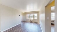 This single-floor unit offers a clean, functional layout with wood-style flooring running consistently throughout all rooms, lending a cohesive and contemporary feel to the space. The entry area provides immediate access to a double-door closet, offering practical storage upon arrival.

The main living area is generously proportioned, featuring neutral-toned walls, bright windows with urban views of the surrounding cityscape, and a wall-mounted HVAC unit that ensures year-round climate control. Natural light fills the room, highlighting the smooth, light-toned flooring and clean white baseboards.

The galley-style kitchen is well-appointed with dark espresso cabinetry extending to the upper and lower walls, white countertops, a stone-tile backsplash, a stainless steel sink, and black appliances including a refrigerator, range, and microwave. The layout maximizes efficiency while maintaining an organized aesthetic.

A separate bedroom features its own window with exterior views and a radiator heating unit, providing a quiet and well-lit retreat. The bathroom includes a full soaking tub with a curved shower rod, white subway tile surround, classic hexagonal floor tile, and brushed nickel fixtures, completing the unit with timeless, functional design.