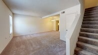 This two-story townhome at The Glen Townhomes in Memphis, Tennessee offers a functional and straightforward layout across two levels. The main floor features a generously sized living area with neutral-toned carpet, a textured ceiling, and a window that brings in natural light. The living space opens toward a dining area illuminated by a chandelier, which connects directly to the galley-style kitchen. The kitchen is equipped with warm wood cabinetry, laminate countertops, a built-in desk or breakfast bar, and black appliances including a range, refrigerator, and dishwasher, all set atop light-toned flooring.

Upstairs, the carpeted bedrooms are well-proportioned and bright, each featuring textured ceilings and ample wall space. One bedroom includes access to a walk-in closet with built-in shelving and hanging rods, offering practical storage. A hallway connects the upper-level rooms seamlessly. The bathrooms feature white tile tub-shower surrounds, standard fixtures, and light tile flooring, presenting a clean and functional design. Throughout the home, a consistent neutral color palette and straightforward finishes create a cohesive, easy-to-personalize living environment.
