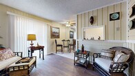 Located at 400 W Central Ave in Wichita, Kansas, this one-bedroom, one-bathroom unit offers a thoughtfully organized single-floor layout that maximizes every square foot. The living room features rich wood-style flooring, vertical blinds allowing natural light to filter in, and a textured ceiling with a ceiling fan. A distinctive vertical-panel accent wall with a pass-through window connects the living area to the kitchen, creating an open and communicative feel between spaces. The dining area, finished with light tile flooring, comfortably accommodates a small bistro-style table and chairs beneath a ceiling fan, and flows directly into the compact kitchen. The kitchen is efficiently equipped with white cabinetry, a full-size refrigerator, electric range, built-in microwave, and a dishwasher, all arranged for practical use. The bedroom provides a cozy retreat with wood-style flooring, warm neutral walls, and ample space for a full bedroom set, complemented by a closet for storage. The bathroom features tile flooring, a tiled tub-shower combination with decorative border accents, a vanity, and clean, functional finishes throughout. Together, the rooms form a cohesive, well-appointed living space suitable for comfortable everyday living.