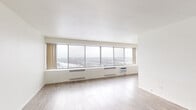 Located at 740 Mississippi River Blvd S in Saint Paul, Minnesota, this single-floor unit offers a bright, open layout defined by clean white walls and an abundance of natural light. The living area is a standout feature, boasting a wide bank of floor-to-ceiling panoramic windows that span nearly the entire exterior wall, delivering sweeping elevated views of the surrounding cityscape and beyond. Light wood-look flooring runs throughout the main living spaces, contributing to the airy, open ambiance. The kitchen is well-appointed with white cabinetry, granite-style countertops, a mosaic tile backsplash, full-size white appliances including a refrigerator, electric range, and built-in microwave, along with track lighting overhead. The bedrooms feature neutral carpet flooring and are each equipped with generous closet storage, including louvered bifold doors and built-in shelving. Both bathrooms are finished with white tile walls and floors, granite-topped vanities with white cabinetry, and mirrored medicine cabinets. One bathroom includes a glass-enclosed stand-up shower, while the other offers a full tub-shower combination. The overall design is clean, functional, and filled with natural light throughout.