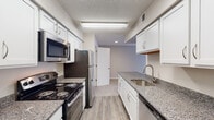 Located at 103 Melville Loop in Chapel Hill, NC, this single-floor residence offers a well-organized layout designed for comfortable everyday living. The galley-style kitchen is a standout feature, outfitted with white shaker cabinetry, granite countertops, stainless steel appliances including a refrigerator, microwave, and dishwasher, and wood-look plank flooring that adds warmth and durability. The living area is generously sized, featuring plush carpeting, neutral-toned walls, and a tiled fireplace that serves as a focal point. A glass door opens to the exterior, allowing natural light to fill the space. The bedrooms continue the neutral palette with soft carpet flooring and ample wall space, offering a calm and functional environment. The bathroom is cleanly appointed with white tile surrounding a full soaking tub and shower, a granite-topped vanity with white cabinetry, and wood-look flooring for a cohesive aesthetic. An additional full bathroom features the same crisp white tile surround. A dedicated laundry area includes an in-unit washer, providing added convenience. Throughout the residence, textured ceilings and clean white trim contribute to a consistent, move-in-ready finish.