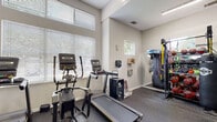 Located at 8531 Summersweet Ln in Raleigh, NC, this single-floor fitness center is thoughtfully designed to support a comprehensive workout experience. The main exercise area features durable speckled rubber flooring throughout, providing both safety and comfort during training sessions. Large windows fitted with horizontal blinds allow generous natural light to fill the space, creating a bright and energizing atmosphere. A ceiling fan overhead contributes to air circulation during intense workouts.

The cardio zone is equipped with multiple treadmills and an elliptical trainer, positioned to take advantage of the natural light from the windows. Opposite the cardio area, a full-length wall mirror expands the sense of space while allowing users to monitor their form. The strength training section is well-stocked with a tiered dumbbell rack, a power rack with barbell and weight plates, and additional resistance machines. A dedicated alcove houses a Matrix functional dual-cable trainer, ideal for versatile strength and rehabilitation exercises.

A separate room adjacent to the main floor serves as a stretch or activity area, featuring hardwood flooring and wall-mounted accessories. The common entry area includes a wall-mounted television, a mirror, and a waste receptacle. The facility's elevated ceilings enhance the open feel of the space, making it a practical and motivating environment for fitness enthusiasts of all levels.