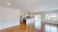 This single-floor unit offers a thoughtfully designed open-concept layout that seamlessly connects the living area, dining space, and kitchen. Rich hardwood-style flooring runs throughout the main living areas, reflecting natural light that pours in through multiple windows and a sliding glass door, creating an airy and welcoming atmosphere.

The kitchen is a standout feature, equipped with a full suite of stainless steel appliances including a French door refrigerator, electric range, over-the-range microwave, and a mosaic tile backsplash. Crisp white shaker-style cabinetry pairs with light countertops and a central island with a sink, providing ample prep and storage space. Pendant lighting above the island adds a refined touch.

The spacious living area benefits from a wall of windows that frame outdoor views and flood the room with natural light. The bedrooms feature plush patterned carpet and generous proportions, with one room offering a stylish barn-style sliding door that leads to a private bathroom complete with a dark wood vanity and large mirror.

The bathrooms are finished with neutral stone-look tile surrounds in the tub/shower combinations, brushed gold hardware accents, and clean white fixtures. A dedicated laundry area is also accessible from within the unit, adding to the overall functionality of this well-appointed space.