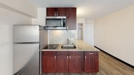 Located at 441 Walina St in the heart of Honolulu, Hawaii, this single-floor unit offers a clean, open layout that maximizes functionality and natural light. The main living area features light wood-style flooring, neutral walls, and a textured ceiling, creating a bright and airy atmosphere. Expansive sliding glass doors span the length of the exterior wall, opening directly onto a private balcony and inviting in ample natural light along with views of the surrounding Waikiki neighborhood, with glimpses of palm trees and neighboring architecture.

The kitchen is thoughtfully designed with rich, dark mahogany-toned cabinetry, granite countertops with a coordinating tile backsplash, a stainless steel sink and microwave, and a full-size refrigerator. The kitchen flows seamlessly into the living space, making it ideal for everyday living.

The bathroom is a standout feature, showcasing a walk-in shower enclosed by a frosted sliding glass door. The shower interior is finished with large-format beige stone tiles accented by a bold, veined marble mosaic border, complemented by a rainfall showerhead for a spa-like experience.

Additional built-in wall shelving in the living area provides practical storage, and a closet offers further organization options. This unit combines modern finishes with a functional layout in one of Honolulu's most vibrant neighborhoods.