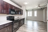 Located on Murphy Street in the heart of Des Moines, Iowa, this efficiently designed single-floor unit offers a thoughtful open-concept layout that maximizes every square foot. The space is characterized by its urban industrial aesthetic, with exposed silver ductwork running along the textured ceiling, adding a distinctive architectural element throughout.

The kitchen is a standout feature, outfitted with rich dark cabinetry, light countertops, and a full suite of black appliances including a refrigerator, electric range, built-in microwave, and dishwasher. A stainless steel sink anchors the workspace, making the kitchen both functional and stylish.

The open living area flows seamlessly from the kitchen, bathed in natural light from a set of tall windows that frame views of the surrounding cityscape. Light wood-look flooring runs throughout the space, complementing the neutral wall tones and creating a clean, modern feel. A ceiling fan adds practical comfort to the living area.

The bathroom is clean and well-appointed, featuring wood-look flooring consistent with the rest of the unit, a dark vanity, and ample wall space. A louvered closet door and an additional walk-in closet provide convenient storage solutions. The overall ambiance is modern, urban, and efficiently arranged for comfortable city living.