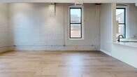 Located at 425 W Lakeside Ave in Cleveland's vibrant Lakeside neighborhood, this unit showcases an industrial-chic aesthetic with thoughtfully updated modern finishes. The open-concept kitchen and living area serves as the heart of the space, where white-painted exposed brick walls create a striking architectural backdrop throughout. Light hardwood flooring runs continuously across the entire unit, adding warmth and cohesion. The living area benefits from tall, black-framed windows that flood the space with natural light and offer urban views of the Cleveland skyline and surrounding cityscape. Exposed wooden ceiling beams add to the loft-inspired character of the space. The kitchen is well-appointed with white shaker-style cabinetry featuring black hardware, white quartz countertops, subway tile backsplash, and stainless steel appliances including a dishwasher, refrigerator, and range. A dedicated closet provides practical storage. The bathroom is cleanly finished with a white vanity with under-cabinet storage, black fixture accents, a mirrored medicine cabinet, and stylish industrial-style lighting. The overall ambiance is a refined blend of historic building character and contemporary design, ideal for those seeking an urban living experience in the heart of Cleveland.