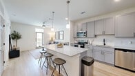 Located at 3755 E McKinney St in Denton, TX, this one-bedroom, one-bathroom unit offers a thoughtfully designed single-floor layout with modern finishes throughout. The open-concept kitchen is a standout feature, equipped with grey shaker-style cabinetry, granite countertops, a stainless steel appliance suite including a French door refrigerator, electric range, built-in microwave, and dishwasher, as well as light wood-look flooring and a peninsula island with bar seating — ideal for casual dining or entertaining. The living room is bright and welcoming, highlighted by a transom-windowed exterior door that invites natural light and outdoor views, complemented by a ceiling fan and light wood flooring. The bedroom features plush carpet, dual windows overlooking the outdoors, a ceiling fan, and direct access to a walk-in closet with built-in shelving. A second closet provides additional storage. The bathroom is finished with the same grey cabinetry and granite countertop vanity, light flooring, and a shower-tub combination. Clean white walls and consistent modern hardware tie the entire space together for a cohesive, contemporary feel.