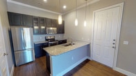 This single-floor residence offers a thoughtfully designed layout with contemporary finishes throughout. The kitchen serves as a central highlight, showcasing deep navy cabinetry—some with glass-front doors—paired with granite countertops, a tile backsplash, and a full suite of stainless steel appliances including a refrigerator, electric range, and built-in microwave. A peninsula with an integrated sink and pendant lighting above anchors the space, providing both functionality and visual appeal. Crown molding and rich hardwood-style flooring add a polished touch to the kitchen and entry areas.

The bedrooms are carpeted and well-lit, each benefiting from natural light through blinded windows. One bedroom features a row of elevated clerestory windows alongside a standard window, creating a bright, airy atmosphere. Ceiling fans are present in the bedrooms for year-round comfort.

The bathrooms feature light wood-look tile flooring and navy vanity cabinetry with granite countertops. The primary bathroom includes a double-sink vanity with a large framed mirror, while a secondary bathroom offers a tub-shower combination with large-format tile surround and a dark wall-mounted storage cabinet. The overall palette of warm grays and navy creates a cohesive, modern aesthetic throughout.