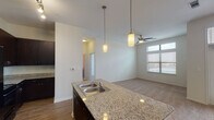 This single-story, one-bedroom, one-bathroom unit in Houston, TX offers a thoughtfully designed open-concept layout that connects the kitchen, dining, and living areas seamlessly. The kitchen serves as a central feature, equipped with dark espresso cabinetry extending to the ceiling for ample storage, granite countertops, black appliances including a French-door refrigerator and range, and a large island with a double stainless steel sink. Pendant lighting and a track lighting system illuminate the space effectively, complementing the wood-style flooring throughout the kitchen area.

The living room transitions to plush carpeting and is brightened by multiple windows, including transom-style upper windows that draw in natural light. A ceiling fan, track lighting, and a glass-paneled door leading to an outdoor area enhance the room's functionality. The bedroom continues the carpeted flooring and features its own ceiling fan, a wide window with outdoor views, and a walk-in closet.

The bathroom includes tile flooring, a full soaking tub with floor-to-ceiling tile surround, granite vanity countertop, dark cabinetry, and direct access to a walk-in closet. The overall palette of neutral tones and contemporary finishes creates a clean, modern ambiance throughout.