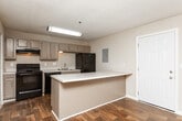 Located at 4946 Snapfinger Woods Dr in Decatur, GA, this single-floor unit offers a well-designed layout with consistent dark hardwood flooring running throughout the entire space, creating a cohesive and polished look.

The open living area is generously sized, featuring neutral beige walls, a textured ceiling, and multiple windows dressed with horizontal blinds that allow ample natural light to filter in. The front entry door opens directly into this welcoming space.

The kitchen is positioned adjacent to the living area and features a functional peninsula with a light countertop surface, ideal for casual dining or meal prep. Gray cabinetry lines the walls, complemented by a mosaic tile backsplash, white countertops, and a full suite of black appliances including a refrigerator, range, and dishwasher. A utility closet with louvered doors provides additional storage within the kitchen area.

A hallway connects the living spaces to the private areas of the unit, including a bedroom that benefits from dual windows offering views to the outside. The bathroom includes a full tub and shower combo with white tile surround, continuing the clean, neutral aesthetic found throughout the home.