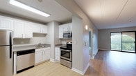 Located at 18 Griffin Terrace in Weymouth, MA, this single-floor unit offers a thoughtfully arranged layout with a clean, contemporary aesthetic throughout. Neutral gray walls and white trim create a cohesive, modern palette that flows from room to room.

The kitchen is a functional highlight, equipped with a full suite of stainless steel appliances including a refrigerator, electric range, built-in microwave, and dishwasher. White cabinetry provides ample storage, while light hardwood-style flooring and recessed fluorescent lighting keep the space bright and practical. The kitchen opens toward a hallway that connects to the main living areas seamlessly.

The living area is generously proportioned, featuring the same light hardwood-style flooring and a sliding glass door that opens to a private balcony overlooking greenery, filling the room with natural light and outdoor views. A wall-mounted air conditioning unit ensures year-round comfort.

The bedroom is carpeted for warmth and comfort, featuring a large window with leafy views, baseboard heating, and access to a walk-in closet with built-in shelving for organized storage.

The bathroom is clean and straightforward, with a full tub and shower combination, wood-style flooring, and brushed nickel fixtures and towel bars throughout.